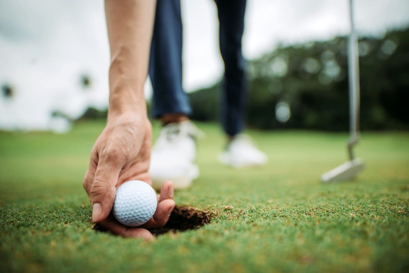 Close-up of hand, golf ball, hole
